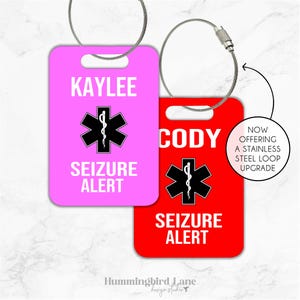 May include: Two personalized luggage tags with a red star of life and the text "Seizure Alert". One tag is pink with the name "Kaylee" and the other is red with the name "Cody".