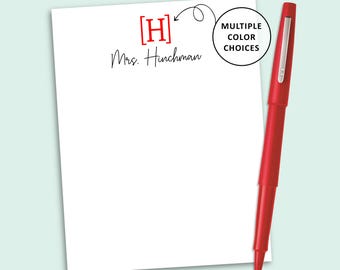 May include: A white notepad featuring a red letter H in brackets and the black script text Mrs. Hinchman. A red pen is positioned to the right of the notepad. A circular graphic with an arrow points to the letter H with the text MULTIPLE COLOR CHOICES.