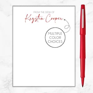 May include: White notepad with the text "From the desk of Krystin Cooper" in red cursive font. A black circle with the text "Multiple Color Choices" is below the name.