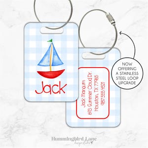 May include: Blue and red gingham luggage tag with a sailboat illustration and the name "Jack" printed in red. The tag also includes a white rectangle with contact information: Jack Mangum, 693 Summer Cloud Dr., Houston, TX 77965, 987.555.4521.