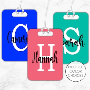 May include: Three luggage tags with different colors and names. The first tag is blue with the name "Cameron" in white letters. The second tag is pink with the name "Hannah" in black letters. The third tag is teal with the name "Sarah" in white letters.  The tags are made of a durable material and have a clear plastic loop for attaching to luggage.