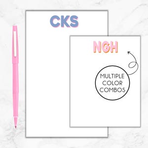 May include: Two white notepads with different colored initials. The top notepad has the initials "CKS" in blue. The bottom notepad has the initials "NGH" in pink, orange, and yellow. The bottom notepad also has a circle with the text "MULTIPLE COLOR COMBOS" and an arrow pointing to the circle.
