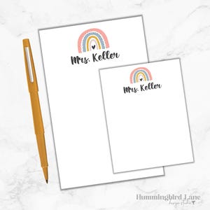 K&ouml;nnte beinhalten: Zwei wei&szlig;e Notizbl&ouml;cke mit einem Regenbogen- und Herzdesign. Der obere Notizblock hat den Text "Mrs. Keller" darauf gedruckt. Der untere Notizblock hat das gleiche Design und den Text "Mrs. Keller" darauf gedruckt.