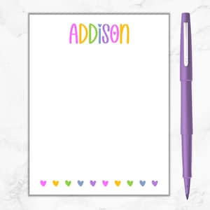 May include: A white notepad with the name "ADDISON" written in rainbow colors. The notepad has a row of colorful hearts at the bottom.