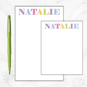 May include: Two white notepad sets with the name "NATALIE" printed in colorful letters. The name is printed in pink, blue, yellow, and green.