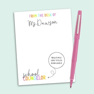 May include: A white notepad with the text FROM THE DESK OF Ms. Dawson in colorful letters, the words school COUNSELOR in colorful script, and a black circular graphic with the text MULTIPLE JOB TITLES AVAILABLE, accompanied by a pink pen.