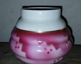 May include: A small, white and pink ceramic vase with a gold trim around the top. The vase has a swirling pattern and pink polka dots.