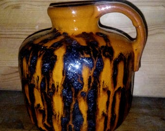 May include: A ceramic pitcher with a handle, featuring a glossy finish. The pitcher has a warm orange base color with dark brown, vertical, dripped patterns. The handle and rim are a lighter shade of orange.