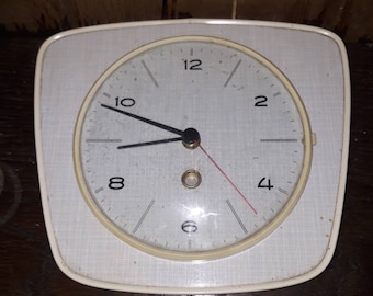 May include: A white square clock with black hands and black numbers on a white face. The clock is set to 10:00.