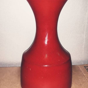 Könnte beinhalten: Eine rote Keramikvase mit breiter Basis und schmalem Hals. Die Vase hat eine glatte, glänzende Oberfläche.