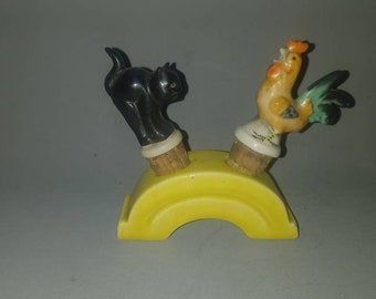 May include: A yellow ceramic bridge with a black cat and a yellow rooster on top. The cat and rooster are both facing the right side of the image.