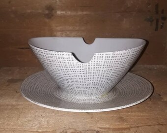 May include: A white ceramic gravy boat with a gray and white geometric pattern. The boat is sitting on a matching saucer.