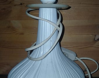 May include: White table lamp with a bulb socket, a round base, and a textured, ribbed design. The lamp has a white cord and a plug. The lamp is on a wooden surface.
