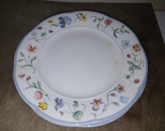 May include: A white ceramic dinner plate with a blue and white floral border. The flowers are in shades of pink, yellow, and blue.