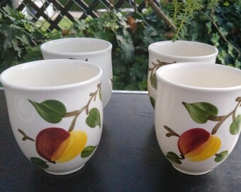 May include: A set of four off-white ceramic mugs featuring a hand-painted design of brown branches with green leaves and round, dual-toned red and yellow fruit. The mugs have a smooth, rounded shape with a wide opening and a tapered base.