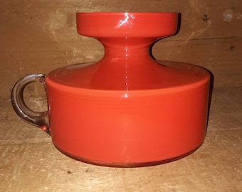 May include: A bright orange glass vase with a clear glass handle. The vase has a wide, round base and a narrow neck.