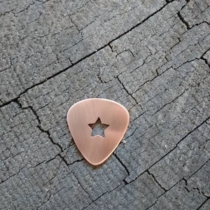 A copper guitar pick with a star-shaped cutout in the center.