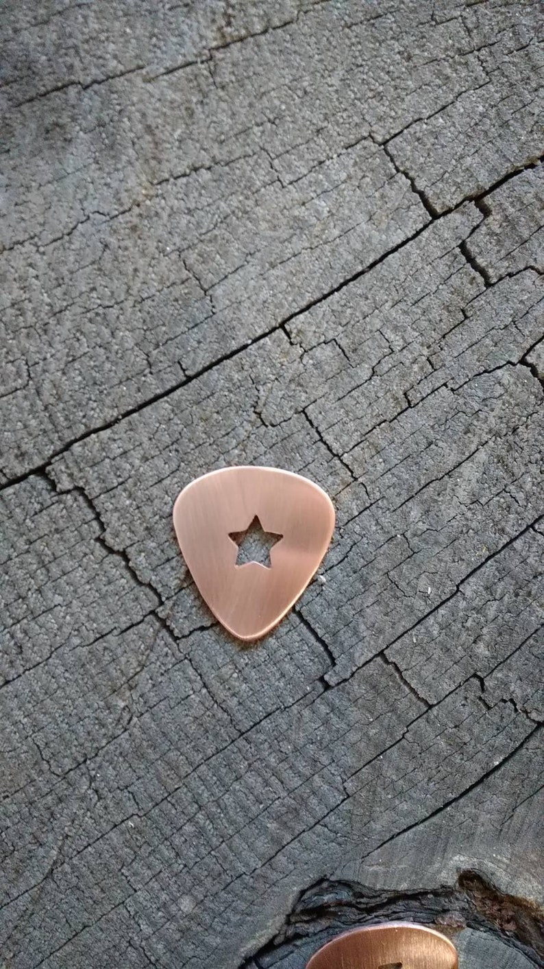 A copper guitar pick with a star-shaped cutout in the center.