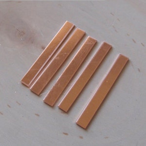 May include: Four thin, rectangular strips of copper metal. The strips are all the same size and are arranged in a row.