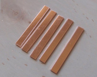 May include: Six copper-colored rectangular bars arranged diagonally on a light-colored wooden surface. The bars are thin and have a slightly reflective surface, suggesting a metallic composition. The arrangement is neat and orderly.