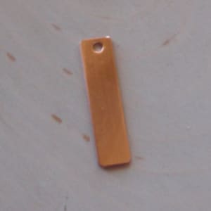May include: A rectangular copper blank tag with a hole at the top. The tag is about 1 inch wide and 2 inches long.