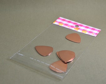 May include: A clear plastic bag containing five copper-colored guitar picks. The picks are in the shape of a triangle and are arranged in a stack.