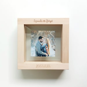 May include: A wooden picture frame containing a photograph of a couple kissing in a snowy woodland. The frame is engraved with the names "Szandi & Gergo" and the date "2022.12.10."