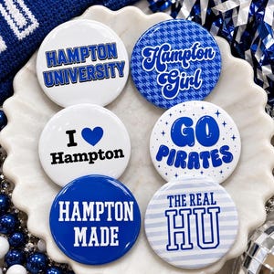 May include: Six circular pinback buttons featuring blue and white designs. The buttons display text including Hampton University, Hampton Girl, I heart Hampton, Go Pirates, Hampton Made, and The Real HU, with various fonts and patterns.