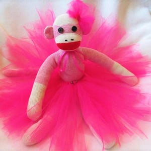 May include: A pink sock monkey wearing a bright pink tulle tutu with a pink bow on its head.
