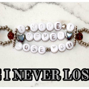 May include: A beaded bracelet with the phrase "I HOPE I NEVER LOSE YOU". The bracelet features silver-colored beads, red beads, and white letter beads. Two silver heart-shaped charms are also included.