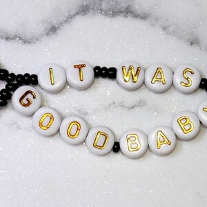 May include: A beaded choker necklace with the phrase "IT WAS GOOD BABY" spelled out in white letter beads with gold lettering. The necklace features black beads with yellow and red accents.