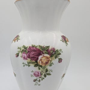 以下が含まれることがあります： 白いセラミック花瓶、フレアトップとスカラップベース、バーガンディ、ピンク、黄色のバラと緑の葉のフローラルパターンで飾られています。 リムとベースは金でトリミングされています。