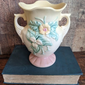 May include: A vintage ceramic vase with a yellow and pink glaze. The vase has two handles and features a floral design with green leaves and yellow and pink flowers.
