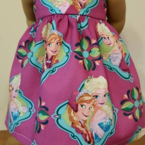 May include: A sleeveless magenta dress featuring a repeating pattern of Elsa and Anna from Frozen. The dress has a scoop neckline and a gathered skirt. The characters are framed in teal and green decorative borders.