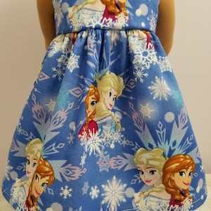 May include: A blue doll dress featuring the characters Elsa and Anna from the movie Frozen, with a snowflake pattern. The sleeveless dress has a gathered waist and is made of fabric.