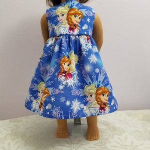 May include: A blue doll dress featuring images of animated characters and snowflakes. The sleeveless dress has a flared skirt and is designed for a doll. The fabric is a vibrant blue with a repeating pattern of the characters and snowflakes.
