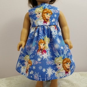 May include: A blue doll dress featuring images of two animated characters, with a snowflake pattern. The sleeveless dress has a fitted bodice and a flared skirt. The characters are blonde and auburn-haired women.