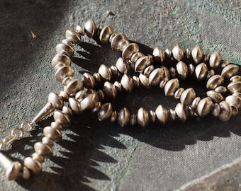 May include: A silver necklace with round beads, each bead has a slightly flattened top. The necklace is made of many beads and is long enough to be worn as a choker or a longer necklace.