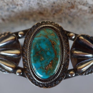 May include: A silver bracelet featuring a turquoise stone set in a silver bezel. The bracelet has a decorative design on the sides.