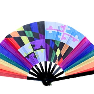 Può includere: Un ventaglio pieghevole con un vivace motivo geometrico multicolore. Il design include segmenti rossi, arancioni, gialli, verdi, blu e viola, con due pannelli azzurri che mostrano un simbolo a croce scuro sia a sinistra che a destra.