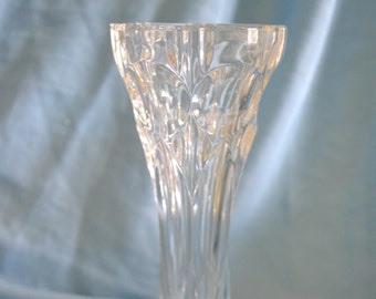 May include: Clear glass bud vase with a flared top and a slender, textured stem. The vase has a round base and is designed with vertical ridges and diamond-shaped patterns. The vase is approximately 8 inches tall.
