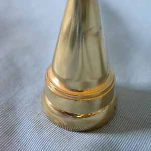 May include: A gold-colored, conical bathroom fixture with a rounded top and a horizontal bar. The fixture has a smooth, polished surface and a decorative base. The overall design is simple and elegant.