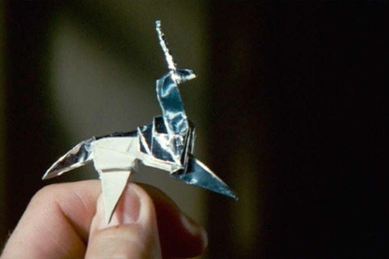 May include: A silver origami unicorn with a pointed horn. The unicorn is folded from a single sheet of paper and is held in a person's hand.