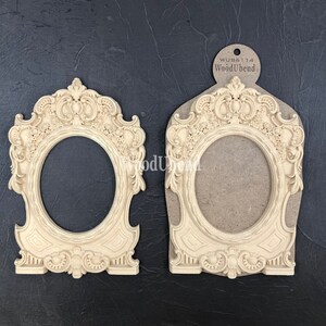 Puede incluir: Dos marcos de fotos de madera de color crema ornamentados, con una abertura ovalada. Los marcos presentan un dise&ntilde;o en relieve detallado con motivos florales y volutas. Los marcos est&aacute;n hechos por WoodUbend y la etiqueta es visible en la imagen.