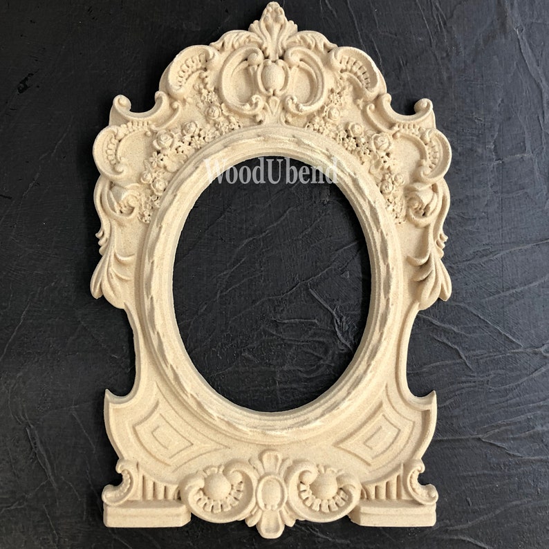 Puede incluir: Un marco de madera de color blanco roto adornado con una abertura ovalada decorativa. El marco presenta intrincados tallados de flores y hojas, y un dise&ntilde;o central con una corona.