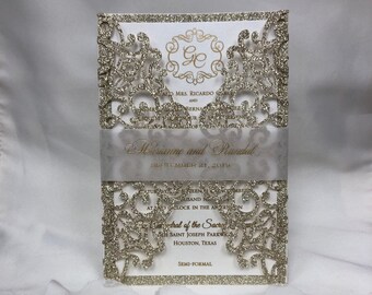 May include: Gold glitter laser cut wedding invitation with a white background. The invitation features a monogram of the letters "G" and "C" in a gold frame. The text on the invitation reads "Marianne and Randal, September 21, 2019, at 4 o'clock in the afternoon, Cathedral of the Sacred Heart, Saint Joseph Parkway, Houston, Texas, Semi-Formal."