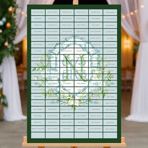 May include: A wedding seating chart displayed on a wooden easel. The chart is a grid of names in small boxes, with a central monogram design in blue and green floral accents. The background is a soft, light blue.