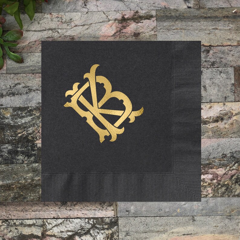 Pu&ograve; includere: Tovagliolo di stoffa nero con un monogramma dorato delle lettere "KB" in un carattere decorativo.