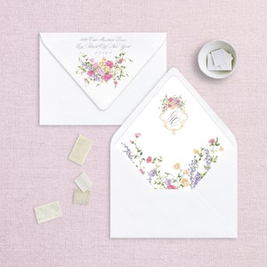 May include: Two white envelopes with floral designs. The envelope on the left has a floral design with pink, yellow, and purple flowers. The envelope on the right has a floral design with pink, yellow, and purple flowers and a monogram in the center. The address on the left envelope reads "629 Oak Mountain Drive, Bay Island City, New York 11101."