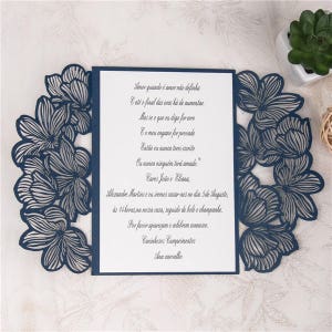 May include: A navy blue wedding invitation with a laser-cut floral design. The invitation text reads: "Amor quando &eacute; amor n&atilde;o definha E at&eacute; o final das eras h&aacute; de aumentar Mas se o que eu digo for erro E o meu engano for provado Ent&atilde;o eu nunca terei escrite Ou nunca ningu&eacute;m teri amado." Caros Jo&atilde;o e Eliana, Alexandre Martins and I are getting married on the 5th of August, at 2 pm at our house, followed by cake and champagne. Please come and celebrate with us. Warmest Regards Ana carvalho